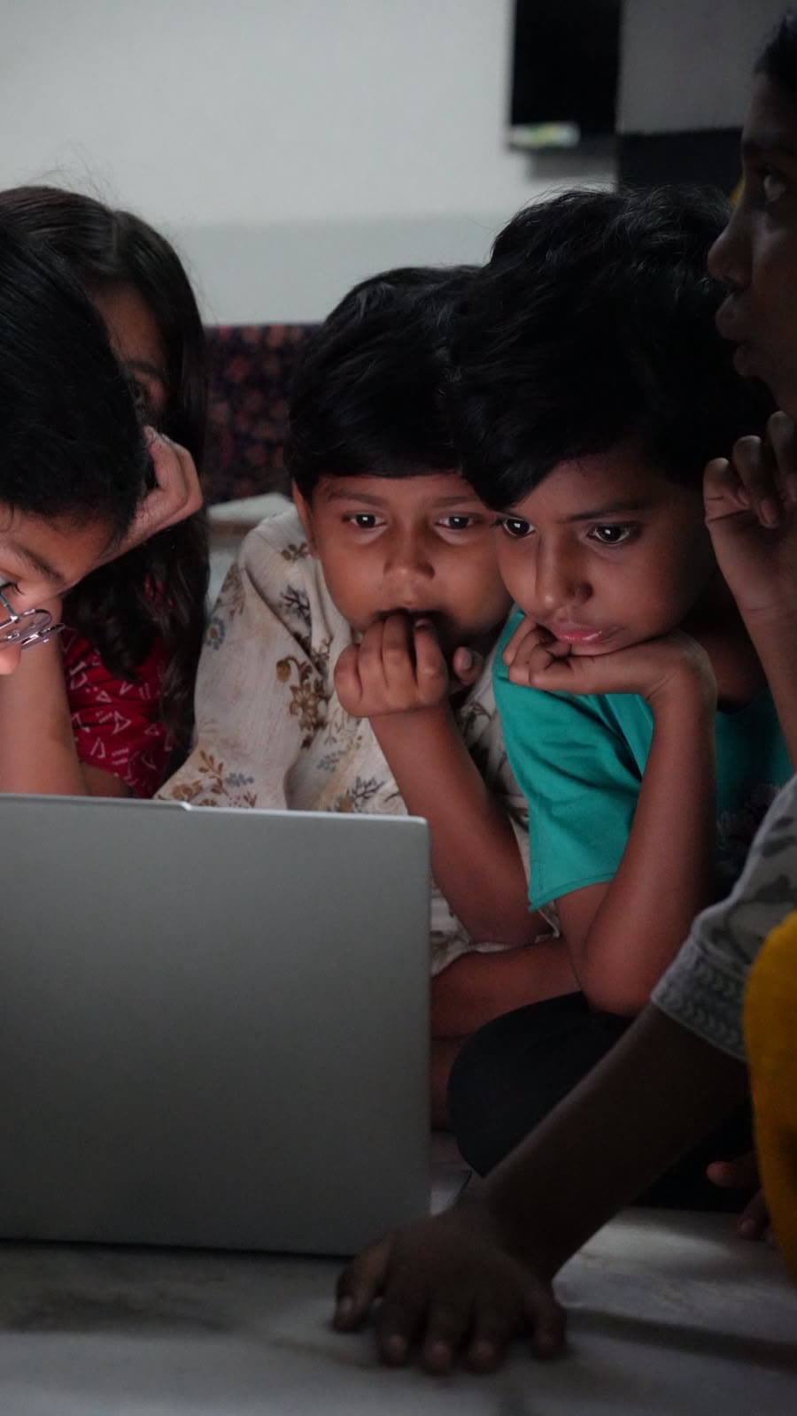Two boys lean in over a laptop, chins in hands.